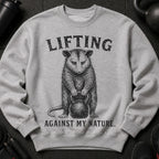 Grey sweatshirt with opossum lifting kettlebell design and text "LIFTING AGAINST MY NATURE."