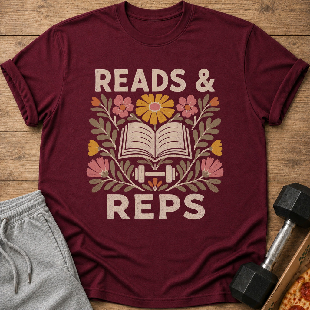A maroon t-shirt with the text READS AND REPS surrounding an open book, dumbbell, and floral graphics.