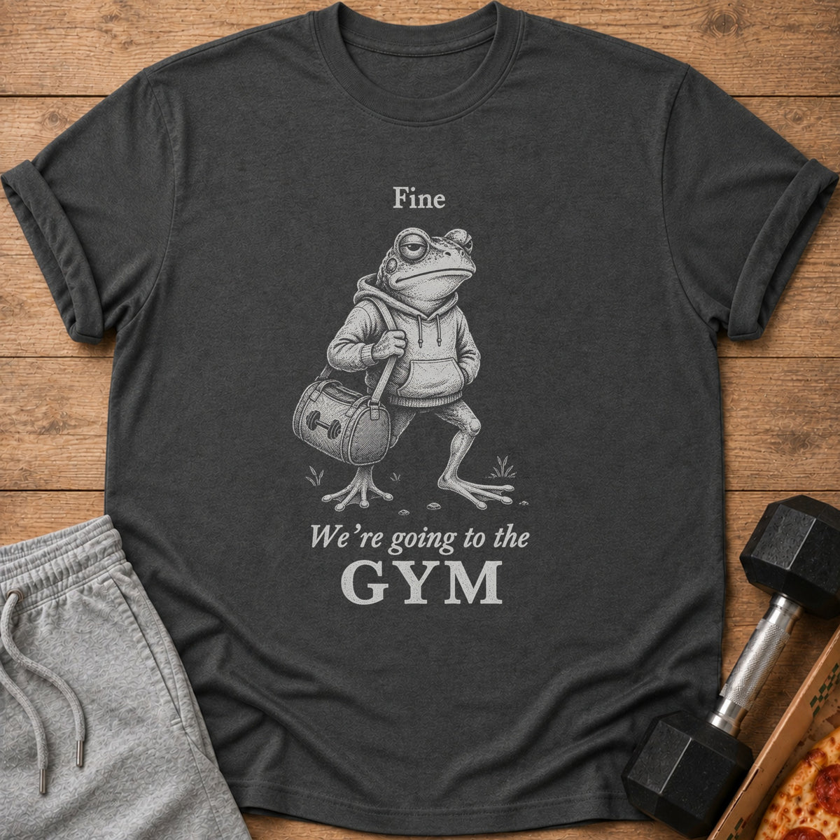 Dark gray t-shirt with a graphic of a frog wearing a hoodie and carrying a gym bag, with text.