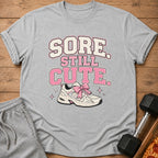 Grey t-shirt with "Sore Still Cute" text and a sneaker with pink bow.