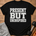 Black t-shirt with distressed text "PRESENT BUT UNINSPIRED", alongside sweatpants and dumbbell.