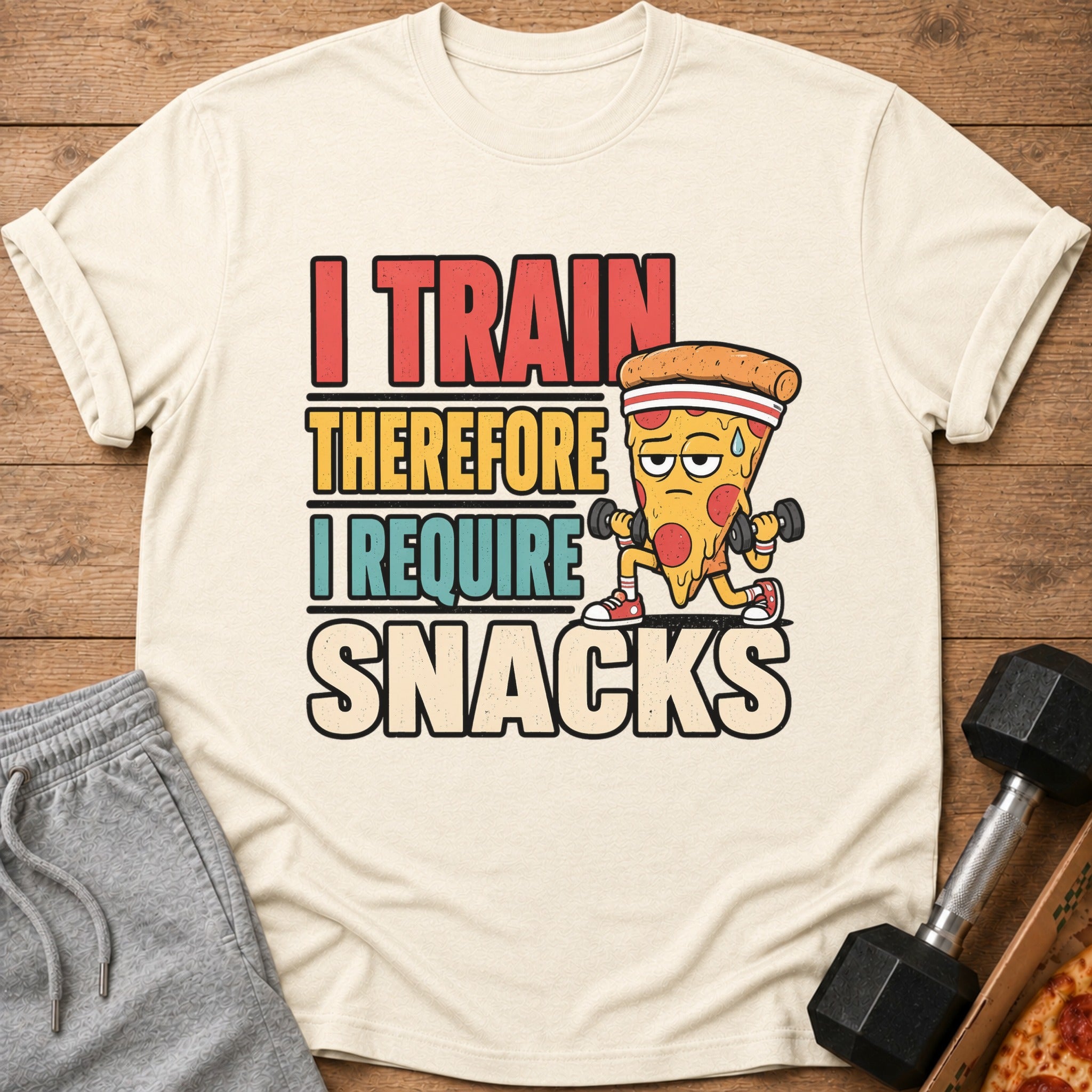 Cream t-shirt with text "I Train Therefore I Require Snacks" and cartoon pizza lifting weights.