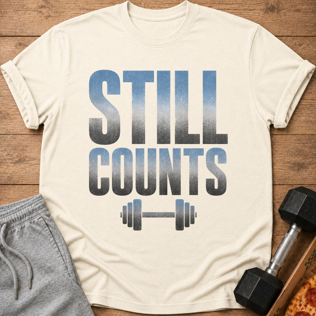 Cream t-shirt with "STILL COUNTS" text and dumbbell graphic, with sweatpants and dumbbell.
