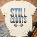 Cream t-shirt with "STILL COUNTS" text and dumbbell graphic, with sweatpants and dumbbell.
