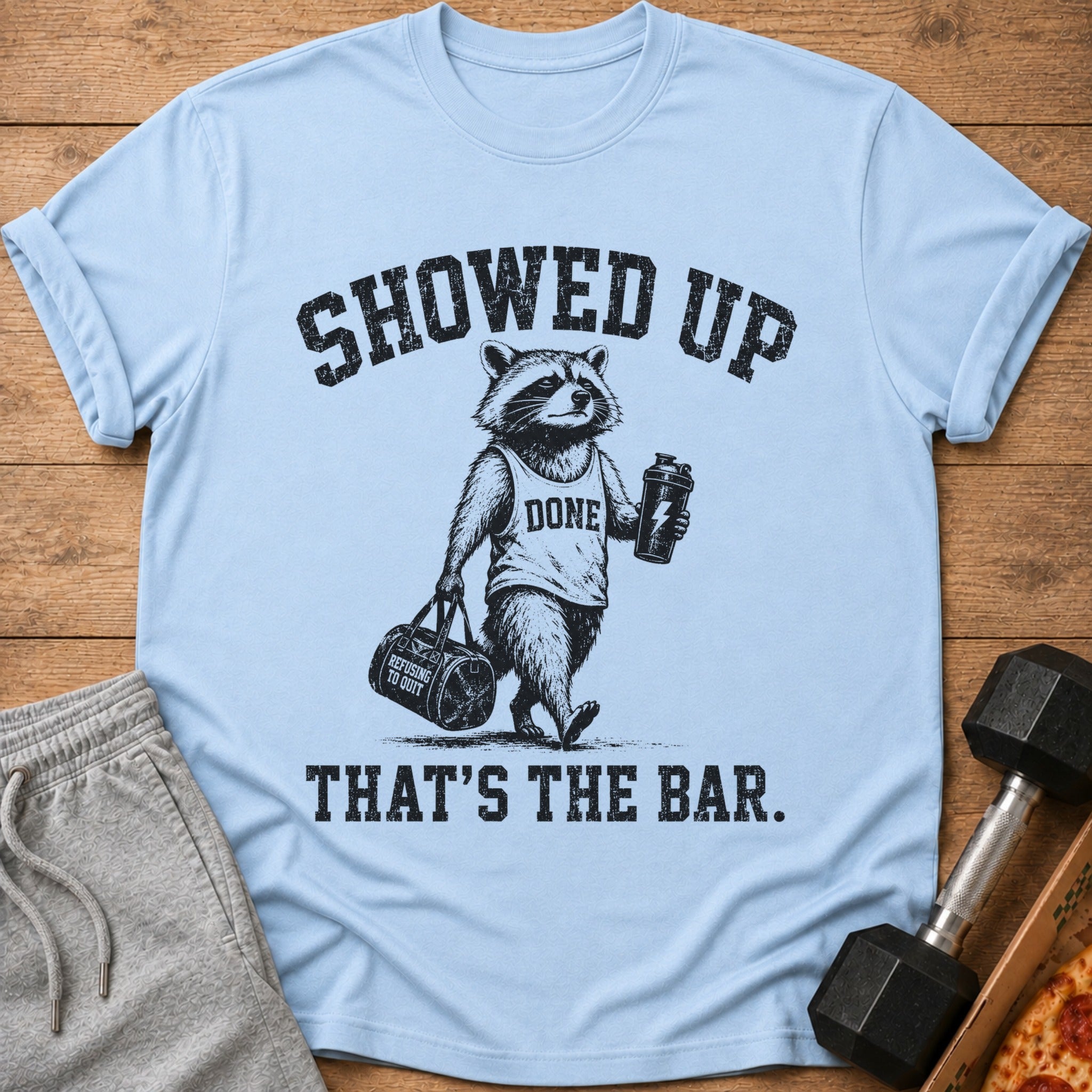 Light blue t-shirt with raccoon graphic: "Showed up, done, that's the bar."