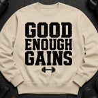 Light tan crewneck sweatshirt with black text "GOOD ENOUGH GAINS" and dumbbell graphic.