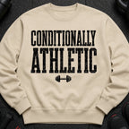 Light beige crewneck sweatshirt with black distressed text "CONDITIONALLY ATHLETIC" and dumbbell graphic.