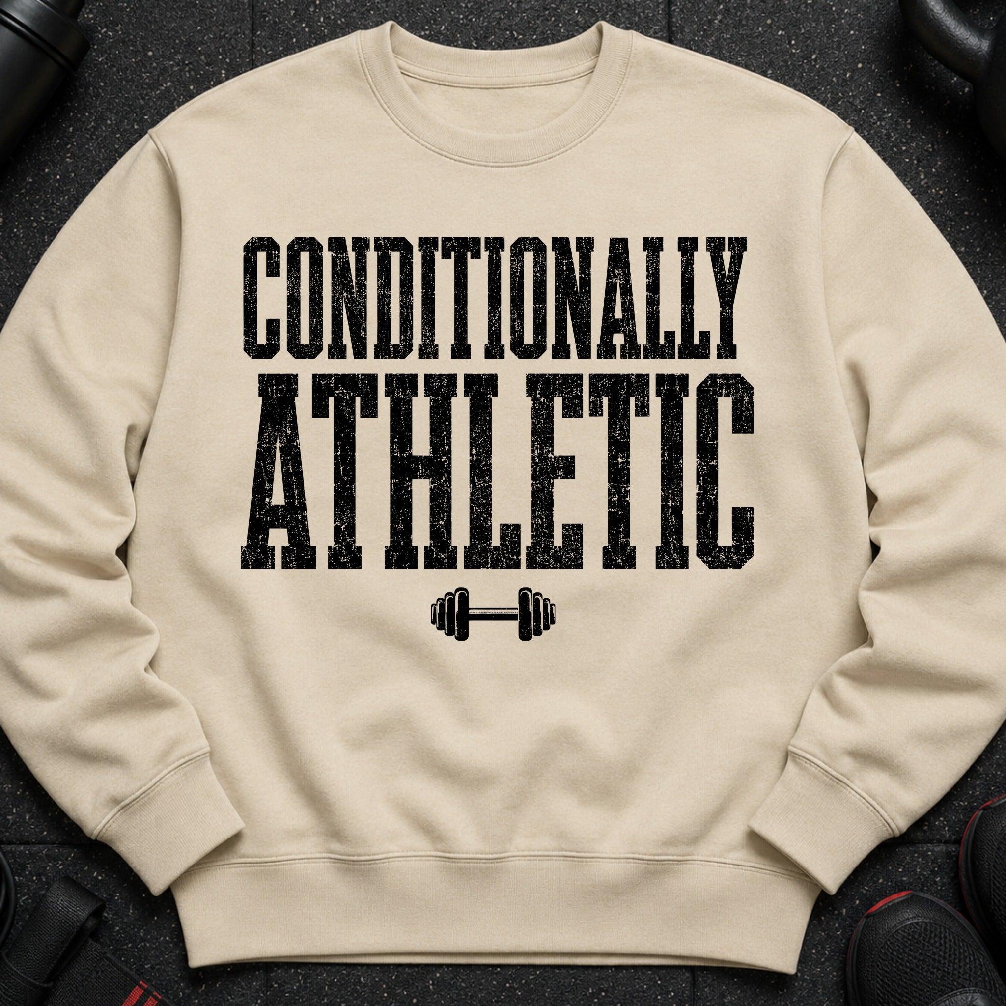 Light beige crewneck sweatshirt with black distressed text "CONDITIONALLY ATHLETIC" and dumbbell graphic.