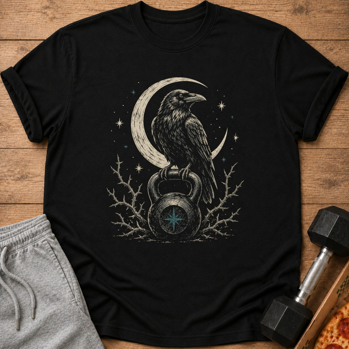 Black t-shirt with a raven perched on a kettlebell under a crescent moon.