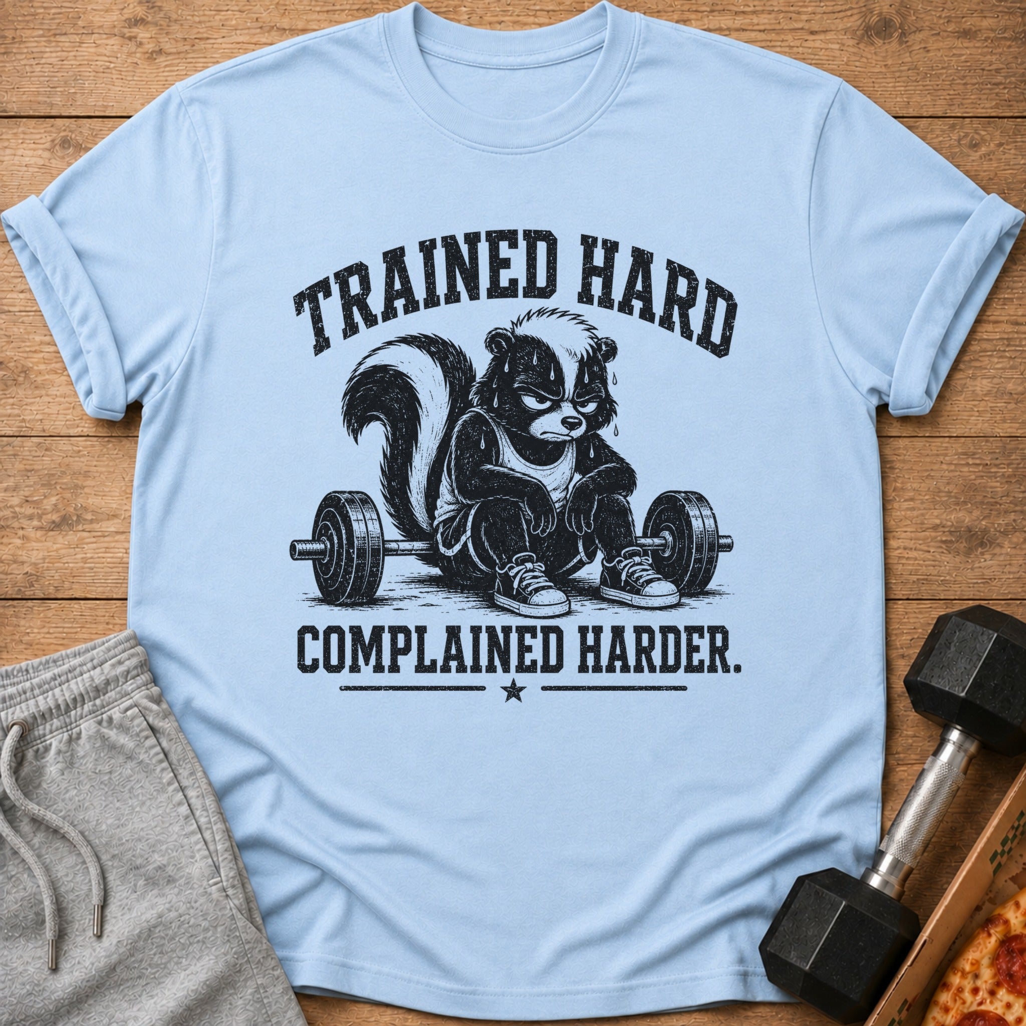Light blue t-shirt with a skunk lifting weights and text "TRAINED HARD COMPLAINED HARDER."