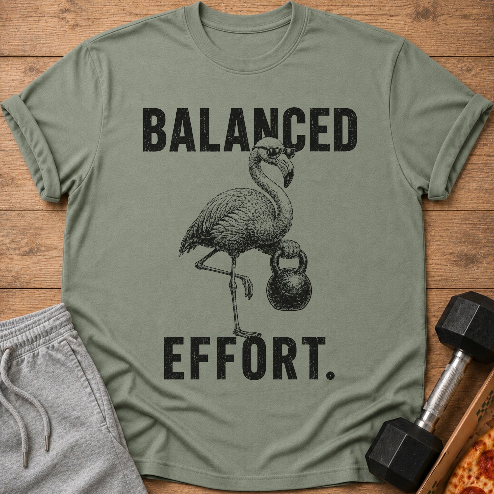 Olive green t-shirt with a flamingo wearing sunglasses holding a kettlebell and text.