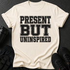 Cream t-shirt with black text reading "PRESENT BUT UNINSPIRED".