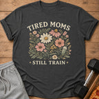 T-shirt with floral design, dumbbell, shaker bottle, and text "TIRED MOMS STILL TRAIN".
