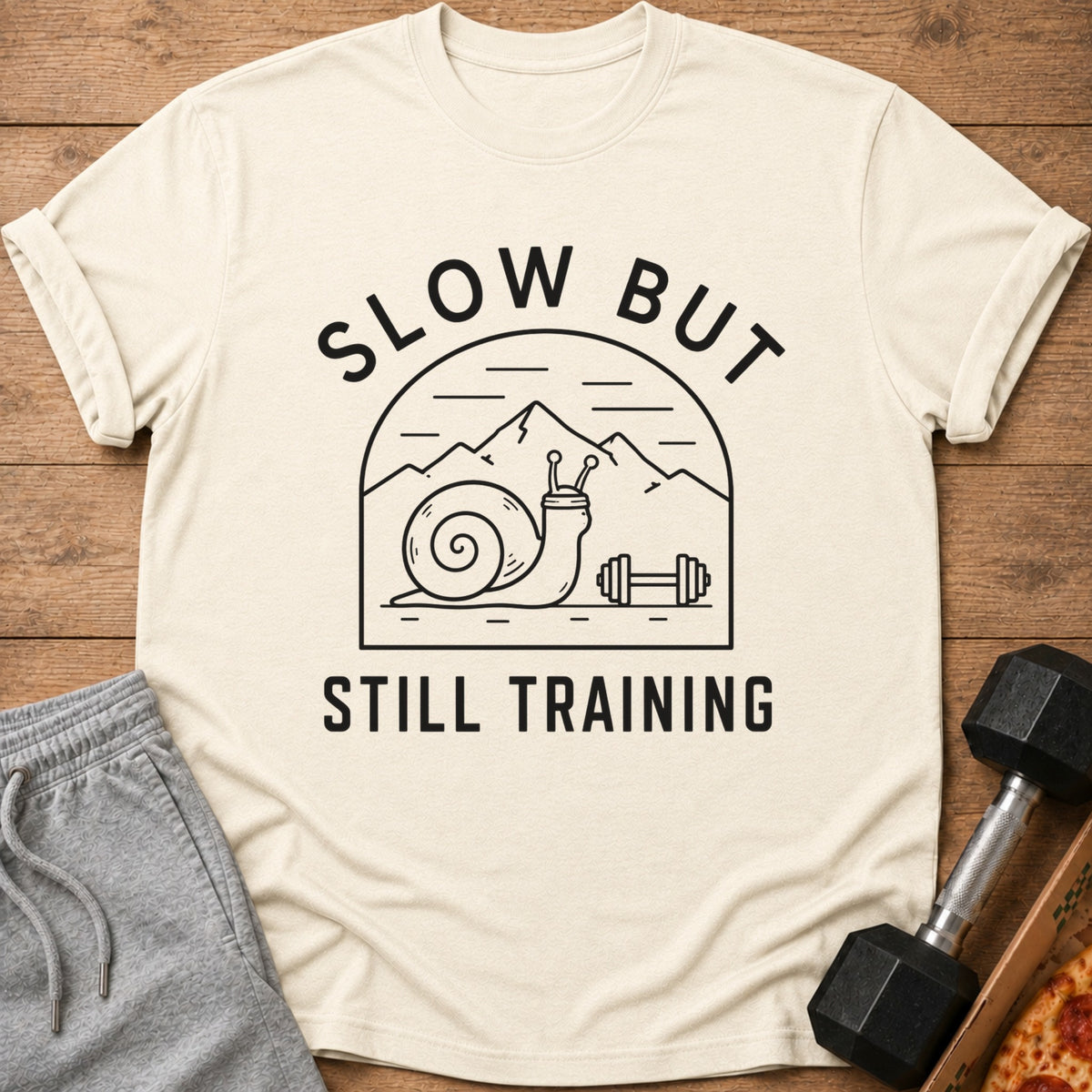 T-shirt with graphic of snail, mountains, and dumbbell with text "SLOW BUT STILL TRAINING".