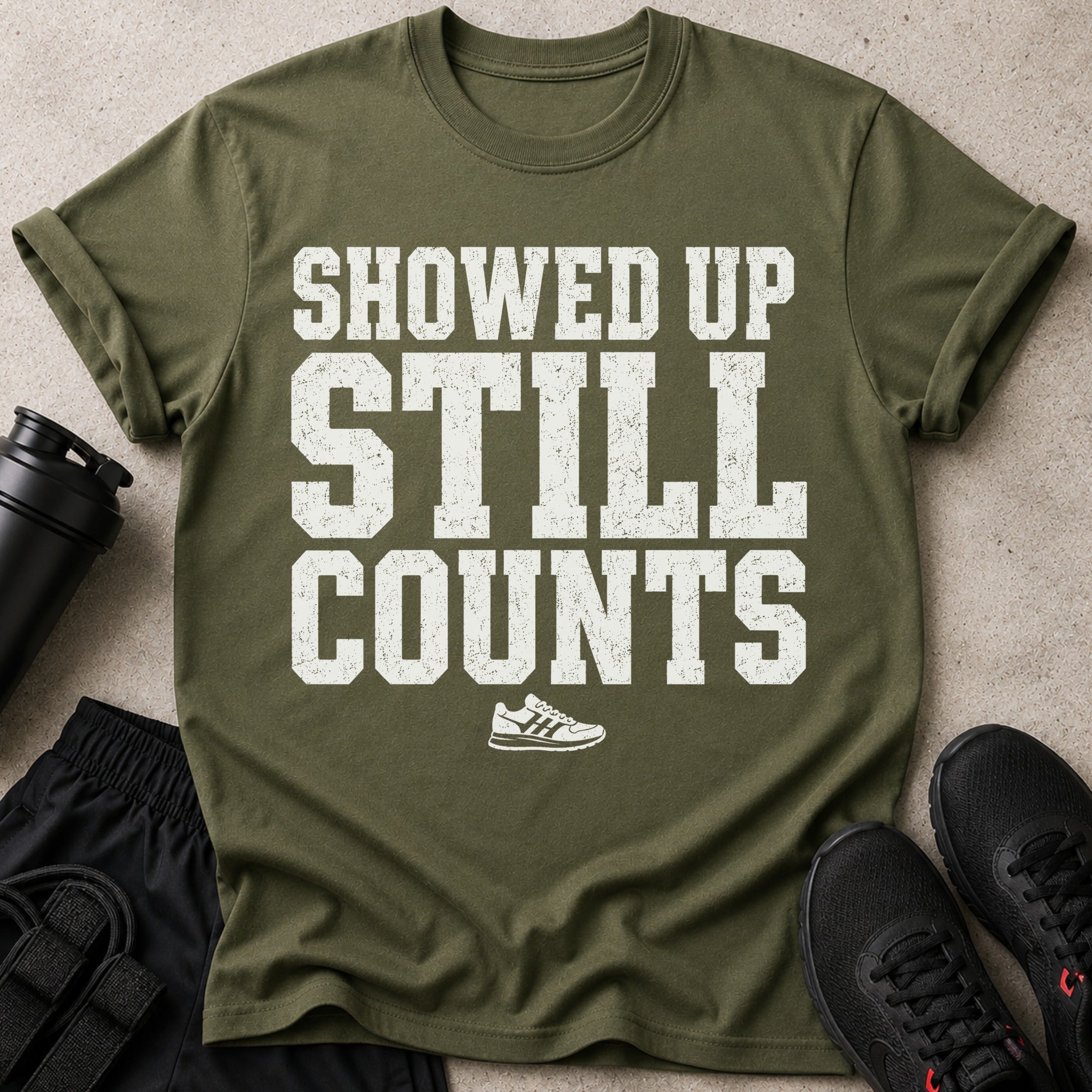 Olive green t-shirt with white text "SHOWED UP STILL COUNTS" and a running shoe graphic.