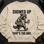 T-shirt with a raccoon mascot holding a gym bag and shaker, with text "SHOWED UP THAT'S THE BAR."