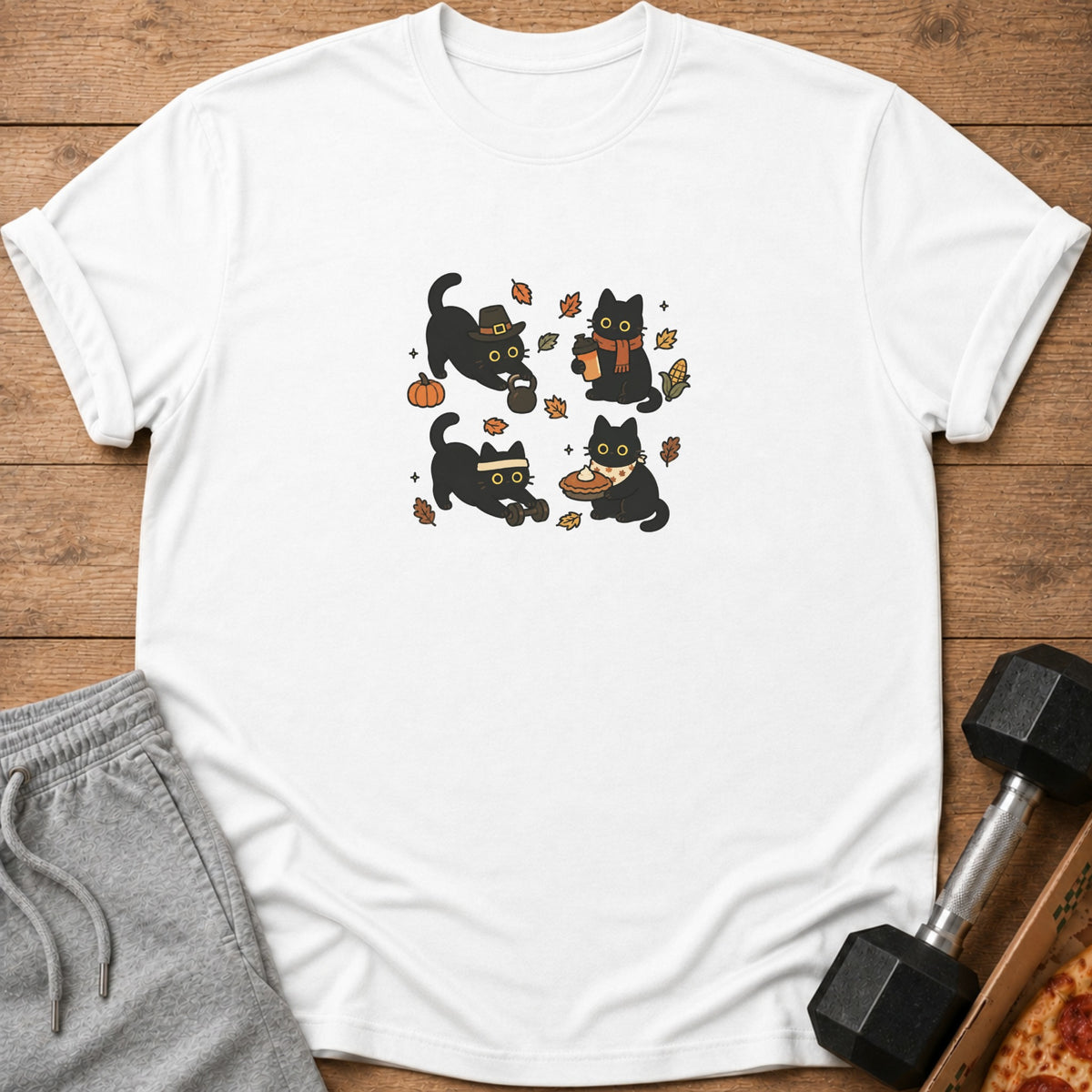 White t-shirt with four cartoon black cats engaged in fall-themed activities.