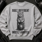 Grey sweatshirt with a cat holding a kettlebell and text: Built Different. Mostly Annoyed.