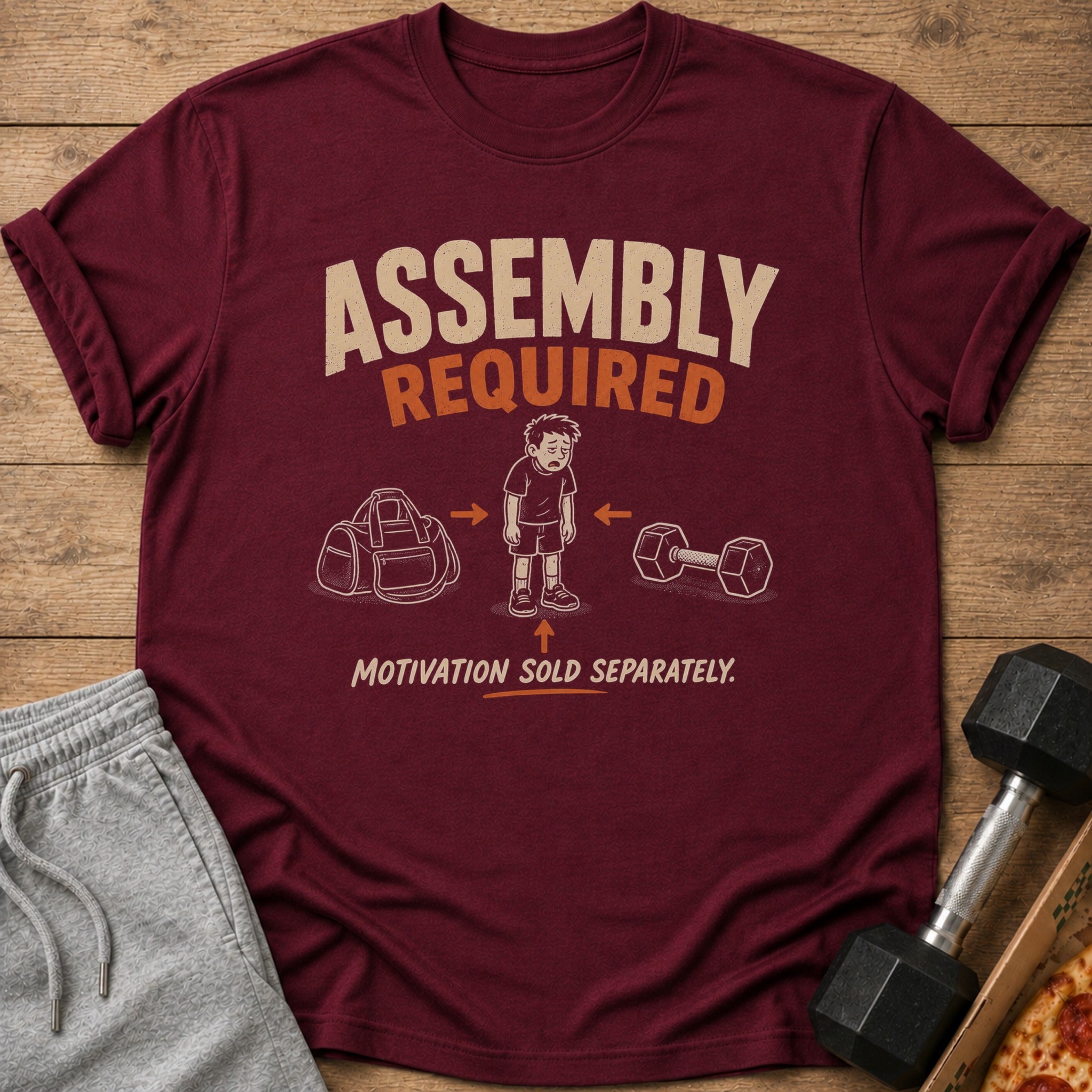 Maroon t-shirt with text "ASSEMBLY REQUIRED MOTIVATION SOLD SEPARATELY" and illustrations.