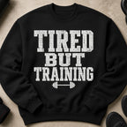 Black sweatshirt with white distressed text "TIRED BUT TRAINING" and barbell graphic.