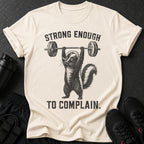 Beige t-shirt with skunk lifting barbell and text "STRONG ENOUGH TO COMPLAIN."
