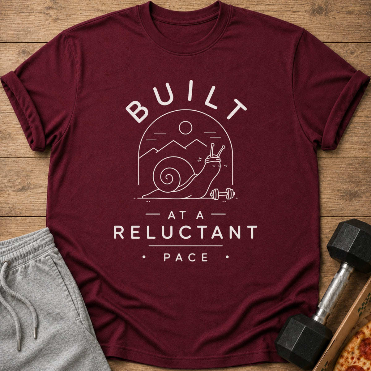 Maroon t-shirt with white text "BUILT AT A RELUCTANT PACE" and a snail graphic.