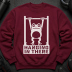 Burgundy sweatshirt with white graphic of frog hanging on bar, text "HANGING IN THERE".