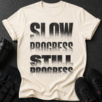 Cream t-shirt with distressed black text reading "SLOW PROGRESS STILL PROGRESS".