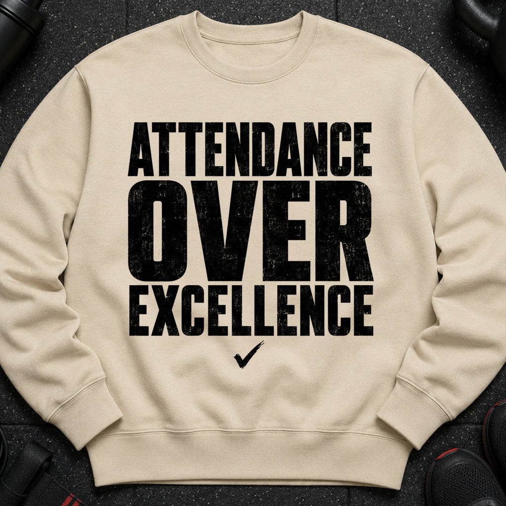 Beige crewneck sweatshirt with black text reading "ATTENDANCE OVER EXCELLENCE" and a checkmark.