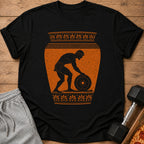 Black t-shirt with orange ancient Greek style design of a man lifting a weight.