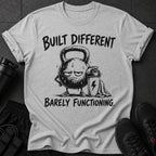 Grey t-shirt with a drawing of a tired kettlebell and the text "BUILT DIFFERENT BARELY FUNCTIONING."