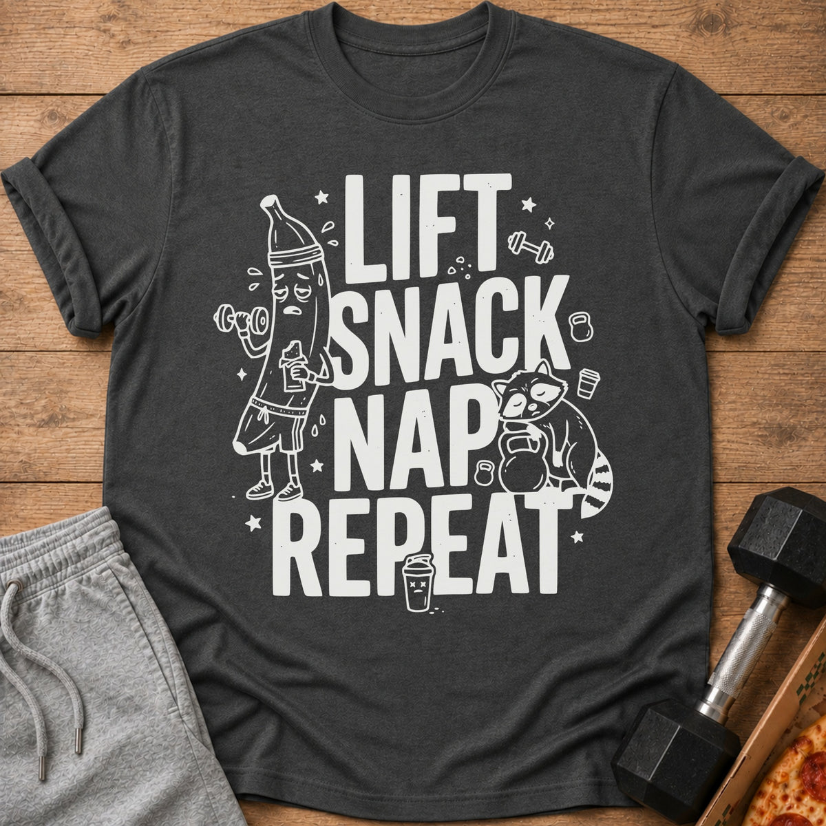 T-shirt with "Lift Snack Nap Repeat" text, cartoon banana lifting weights, sleeping raccoon.