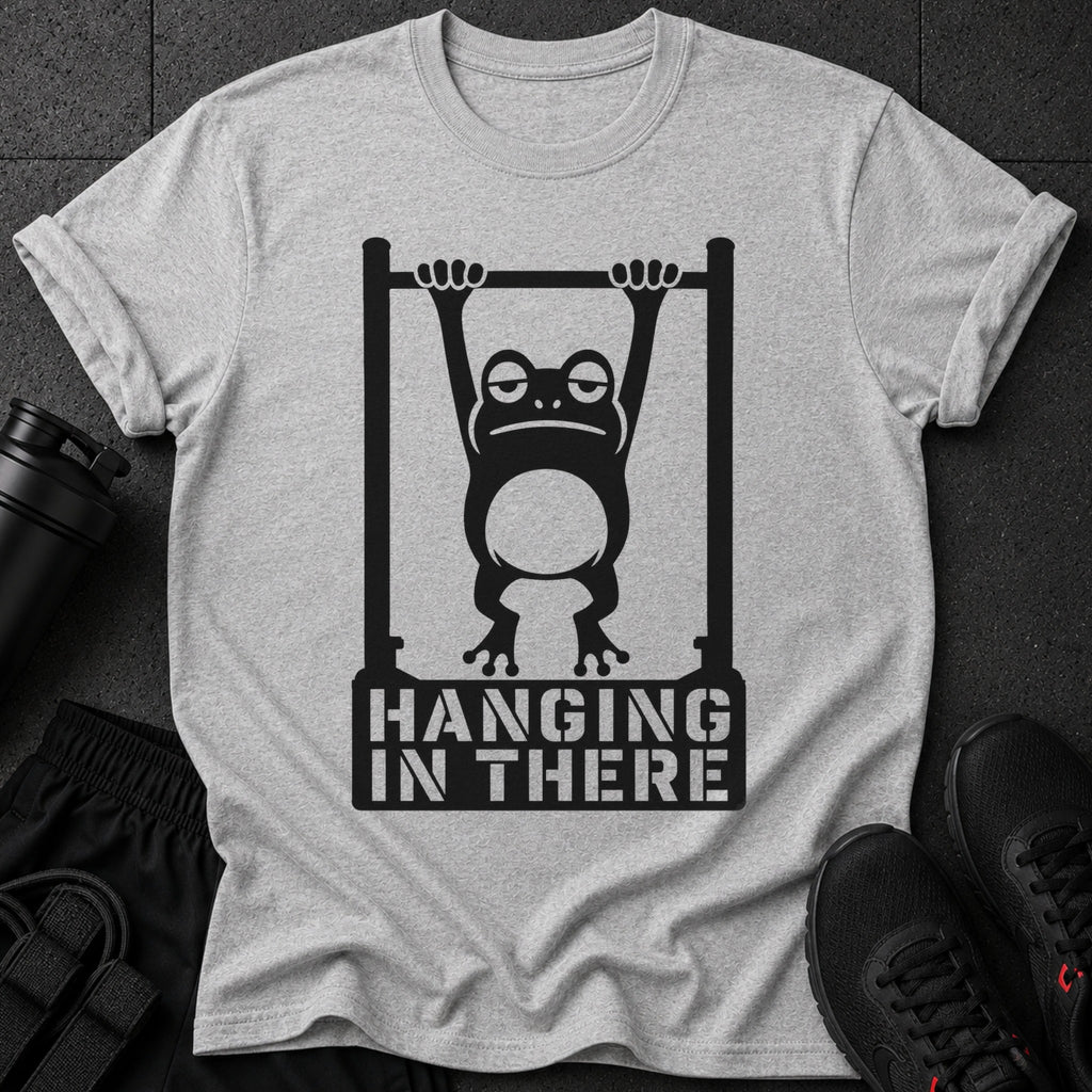Graphic of a frog hanging from a bar with text "HANGING IN THERE" on a grey t-shirt.