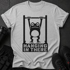 Graphic of a frog hanging from a bar with text "HANGING IN THERE" on a grey t-shirt.