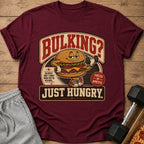 Maroon t-shirt with cartoon burger lifting dumbbell and text "BULKING? JUST HUNGRY."