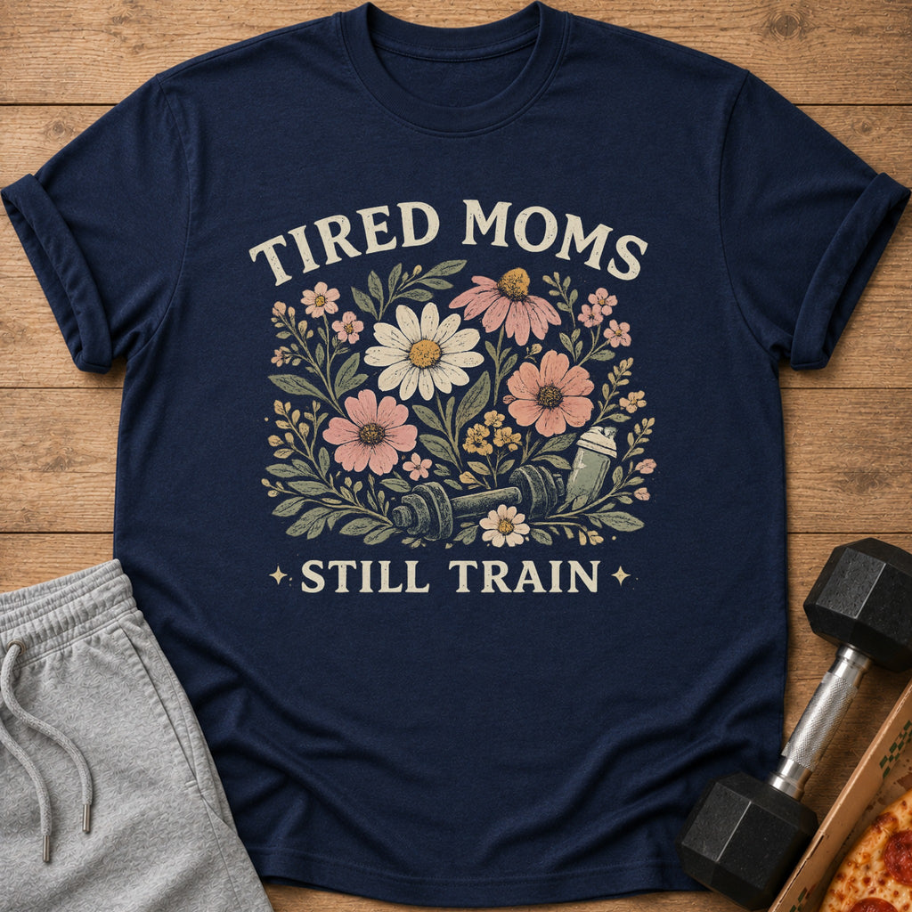 Navy t-shirt with floral design, dumbbell, shaker bottle, and text "TIRED MOMS STILL TRAIN".