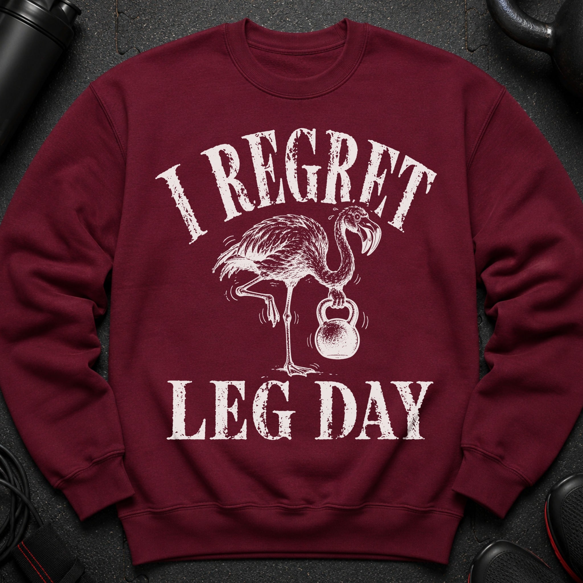 Maroon sweatshirt with distressed graphic of a flamingo lifting a kettlebell and text "I REGRET LEG DAY".