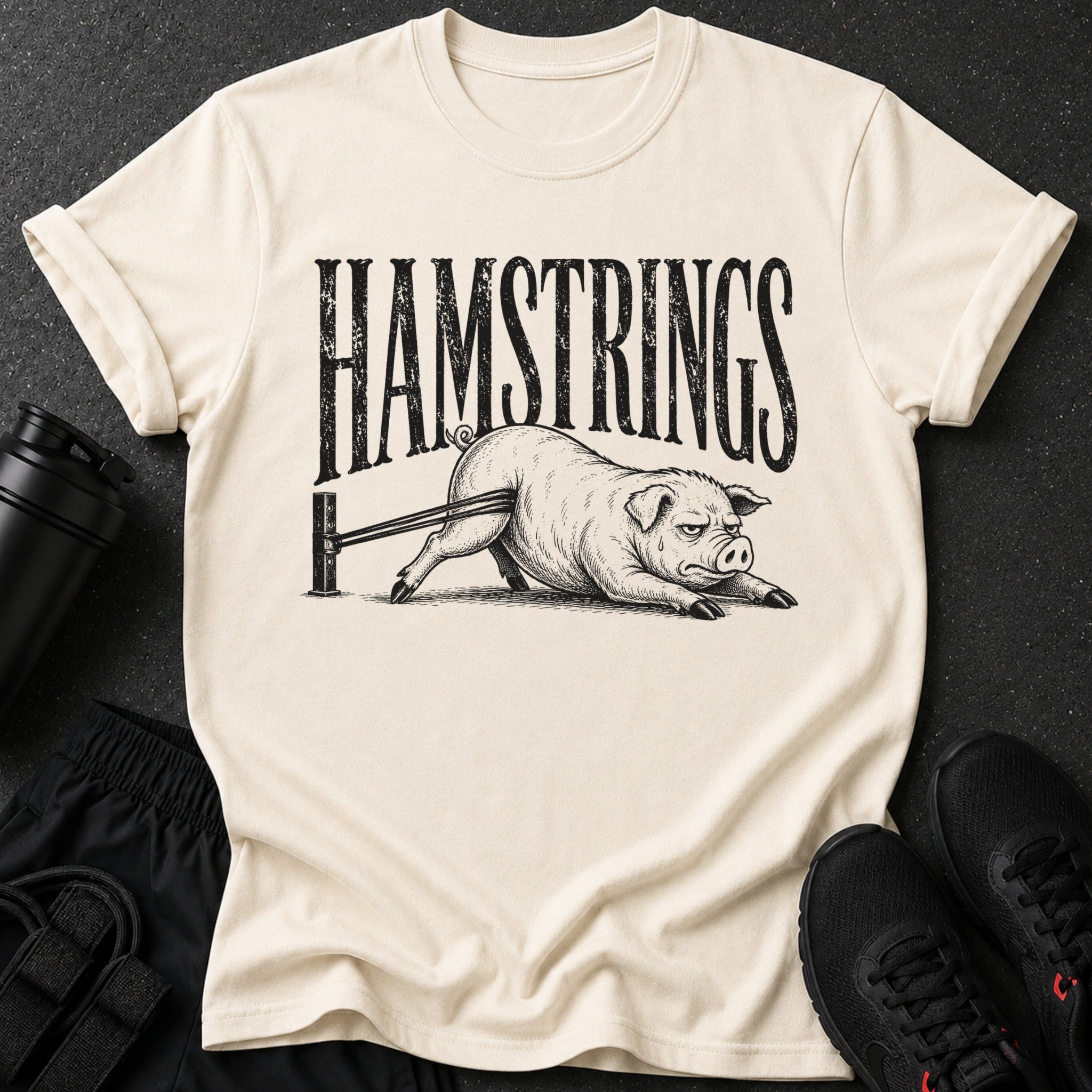 Cream t-shirt with black distressed print "HAMSTRINGS" above a pig with bands around its legs.