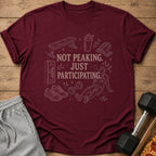 Maroon t-shirt with gym graphics and text "NOT PEAKING. JUST PARTICIPATING."