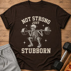 Brown t-shirt with a skeleton lifting weights and the text "Not Strong Just Stubborn".