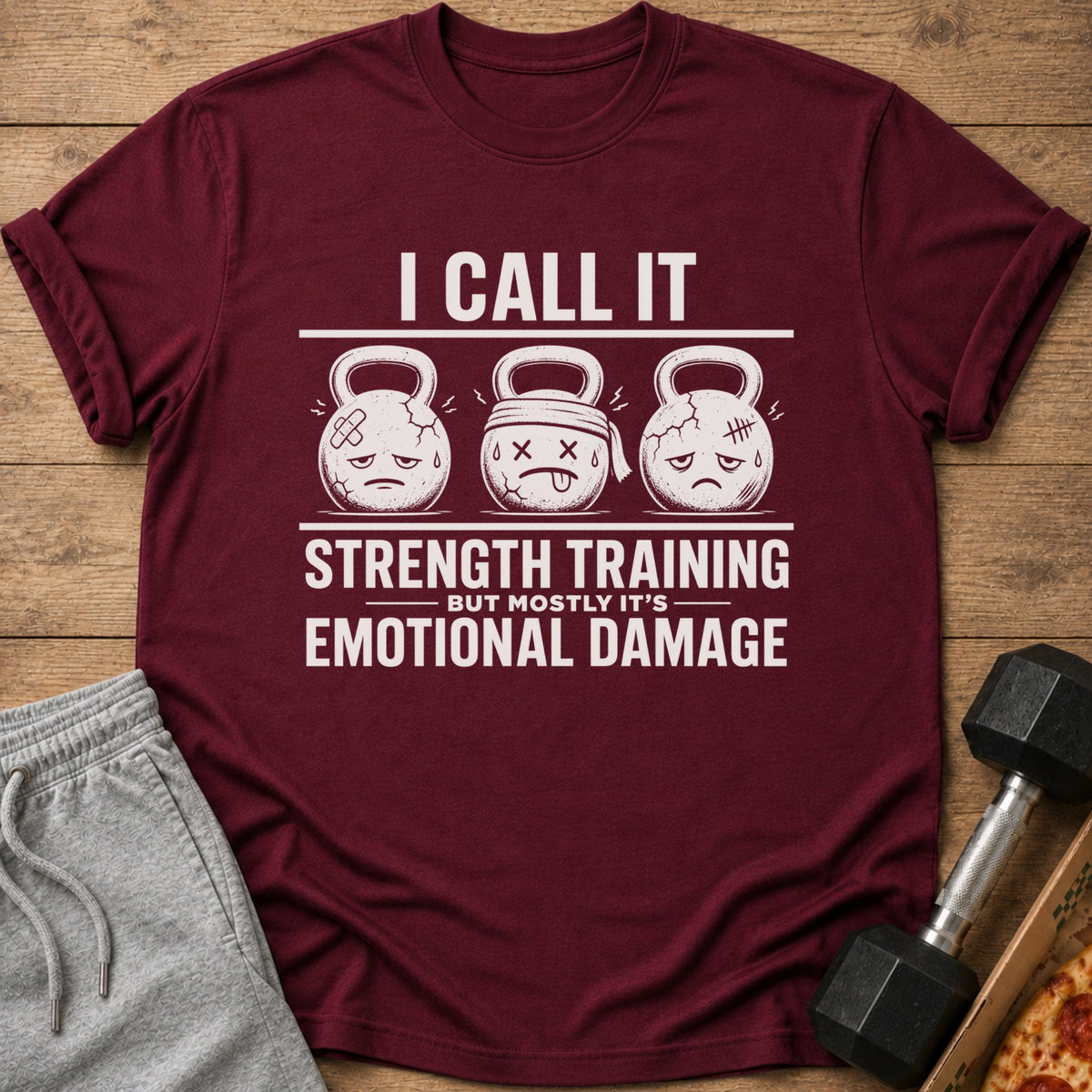 Maroon t-shirt with "I CALL IT STRENGTH TRAINING BUT MOSTLY IT'S EMOTIONAL DAMAGE" text and kettlebells.
