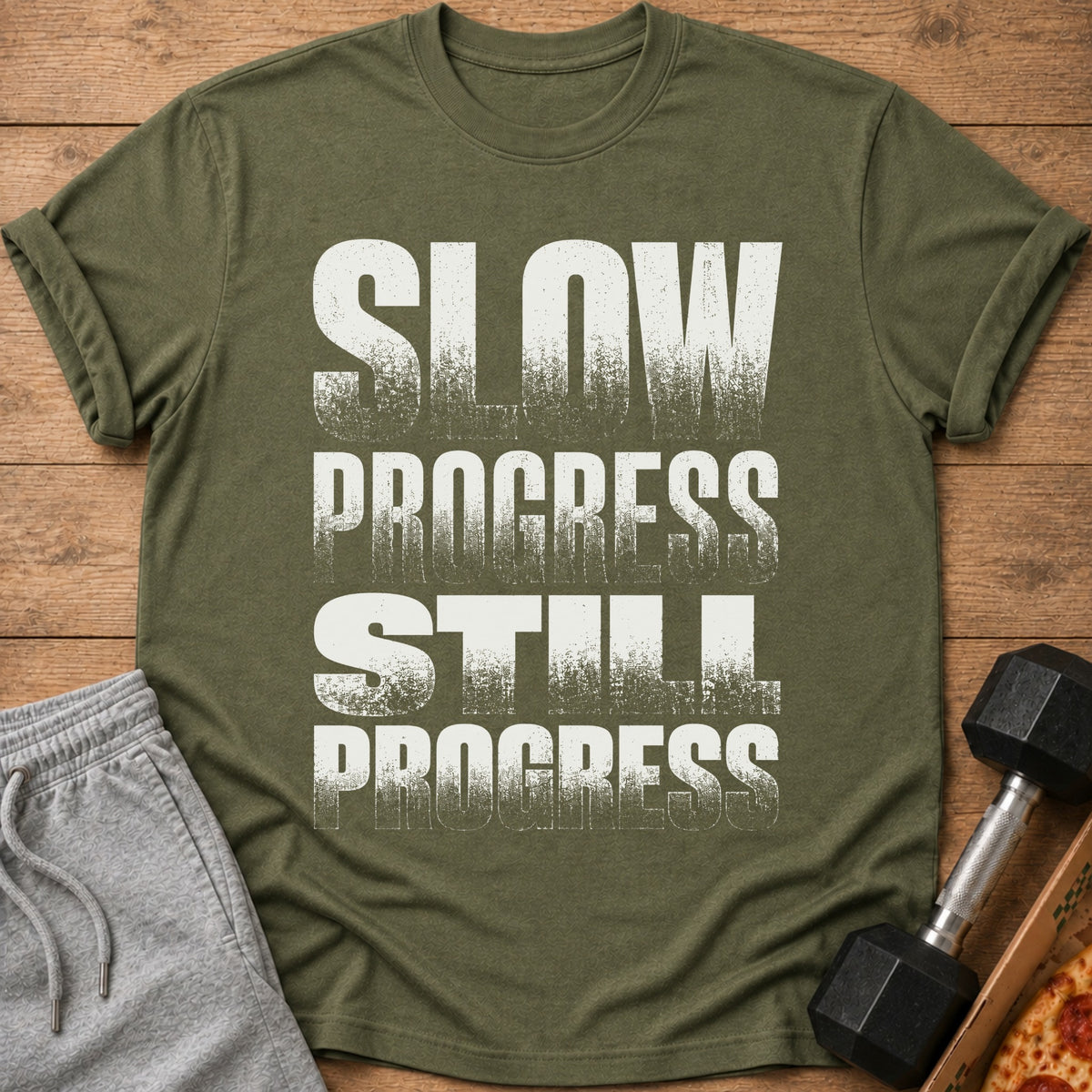 Olive green t-shirt with distressed white text reading "SLOW PROGRESS STILL PROGRESS".