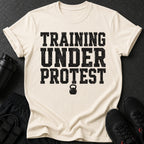 Cream t-shirt with black distressed text "TRAINING UNDER PROTEST" and kettlebell graphic.