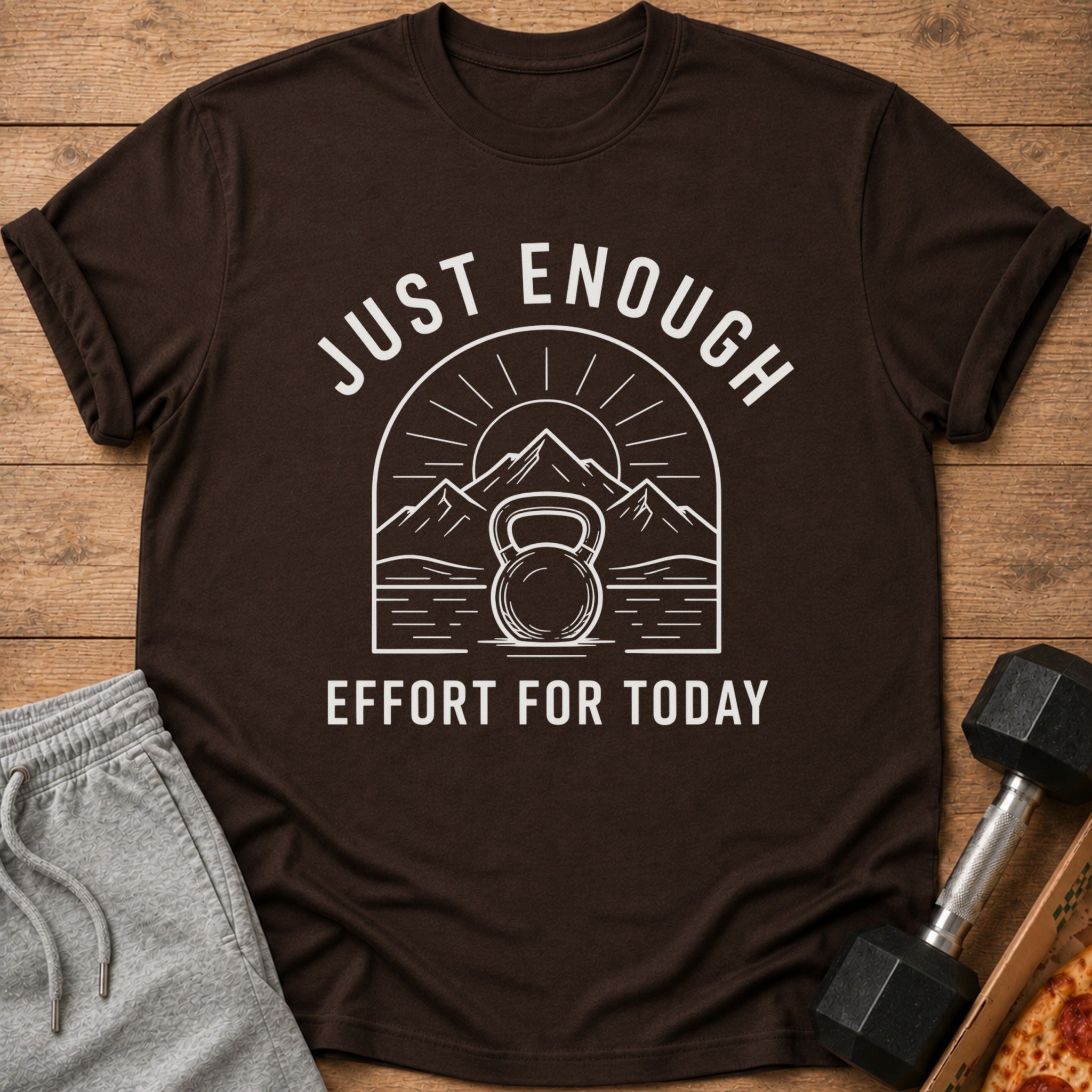Brown t-shirt with white text and graphic of kettlebell, mountains, and sun.