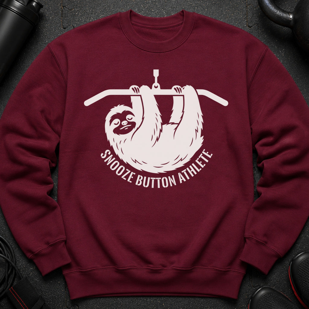 Maroon sweatshirt with a white graphic of a sloth hanging from a bar and the text "Snooze Button Athlete".