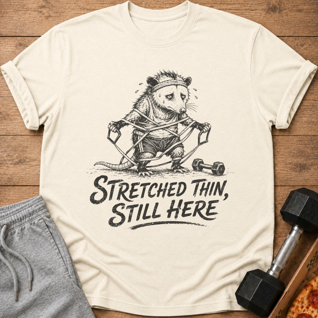 T-shirt graphic of a sweating opossum tangled in resistance bands, with text "Stretched Thin, Still Here".