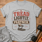 Grey t-shirt with "TREAD LIGHTLY, PARTNER." text and a cowboy hat on a treadmill.