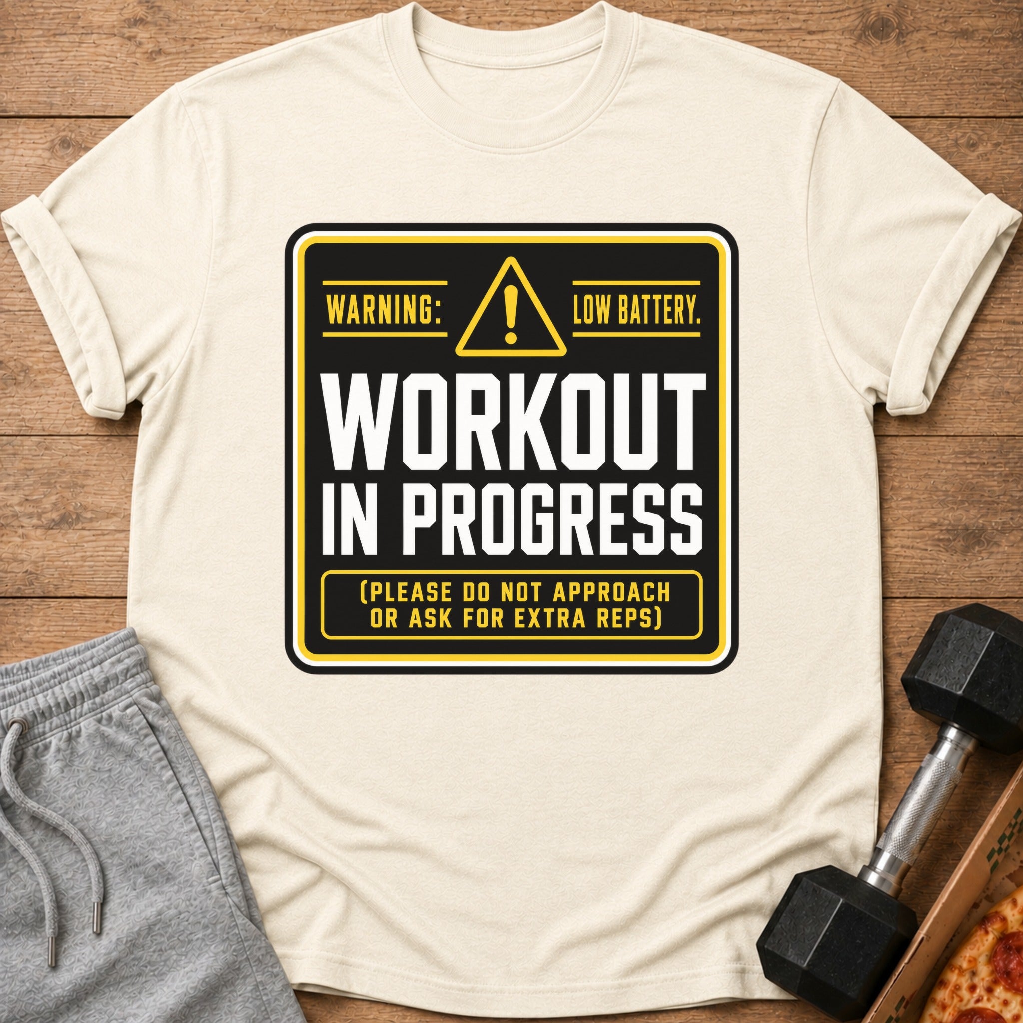 Cream t-shirt with black and yellow "Workout In Progress" graphic about low battery.