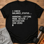 Black t-shirt with text: "CHECK BALANCE_STATUS... WARNING: LIFTING MODE ACTIVE / MOTIVATION SUB-ZERO"