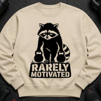 Crewneck sweatshirt with a black graphic of a raccoon holding kettlebells and the text "RARELY MOTIVATED".